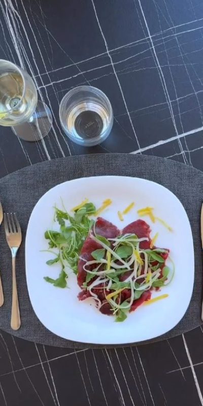 Piatto di carpaccio con insalata su tavolo apparecchiato.