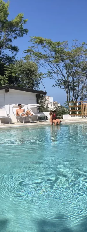 Piscina all'aperto circondata da alberi e sedie a sdraio sotto un cielo azzurro.